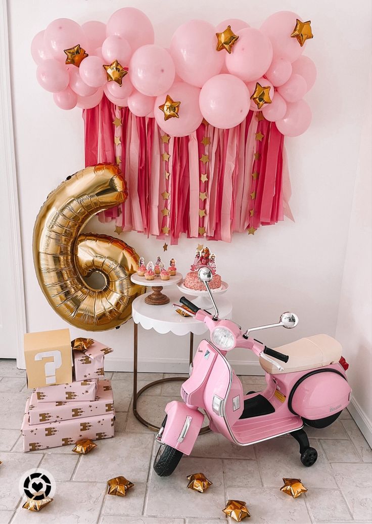 a pink scooter parked next to a table with balloons in the shape of number six