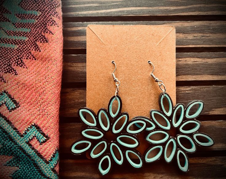 a pair of earrings sitting on top of a wooden table next to a piece of paper