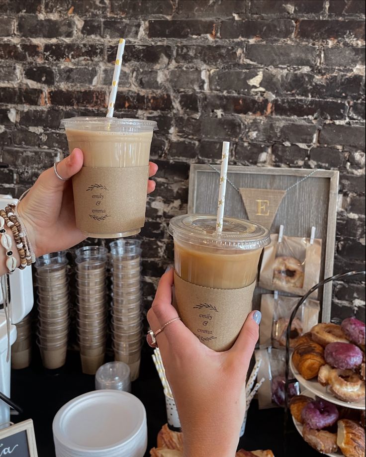 two people holding up drinks in front of doughnuts and pastries on a table