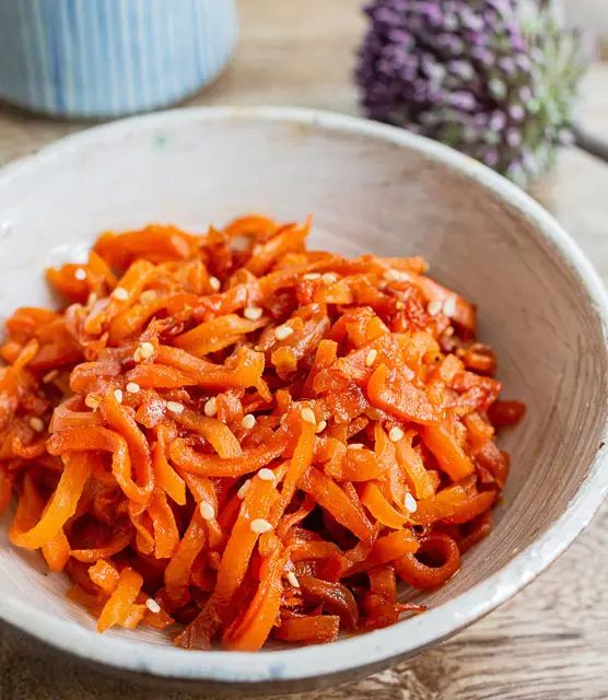 a white bowl filled with carrots on top of a wooden table