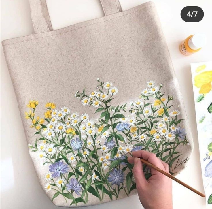 someone is painting flowers on a canvas bag