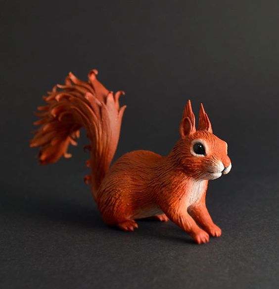 a red squirrel figurine sitting on top of a black table next to a gray background