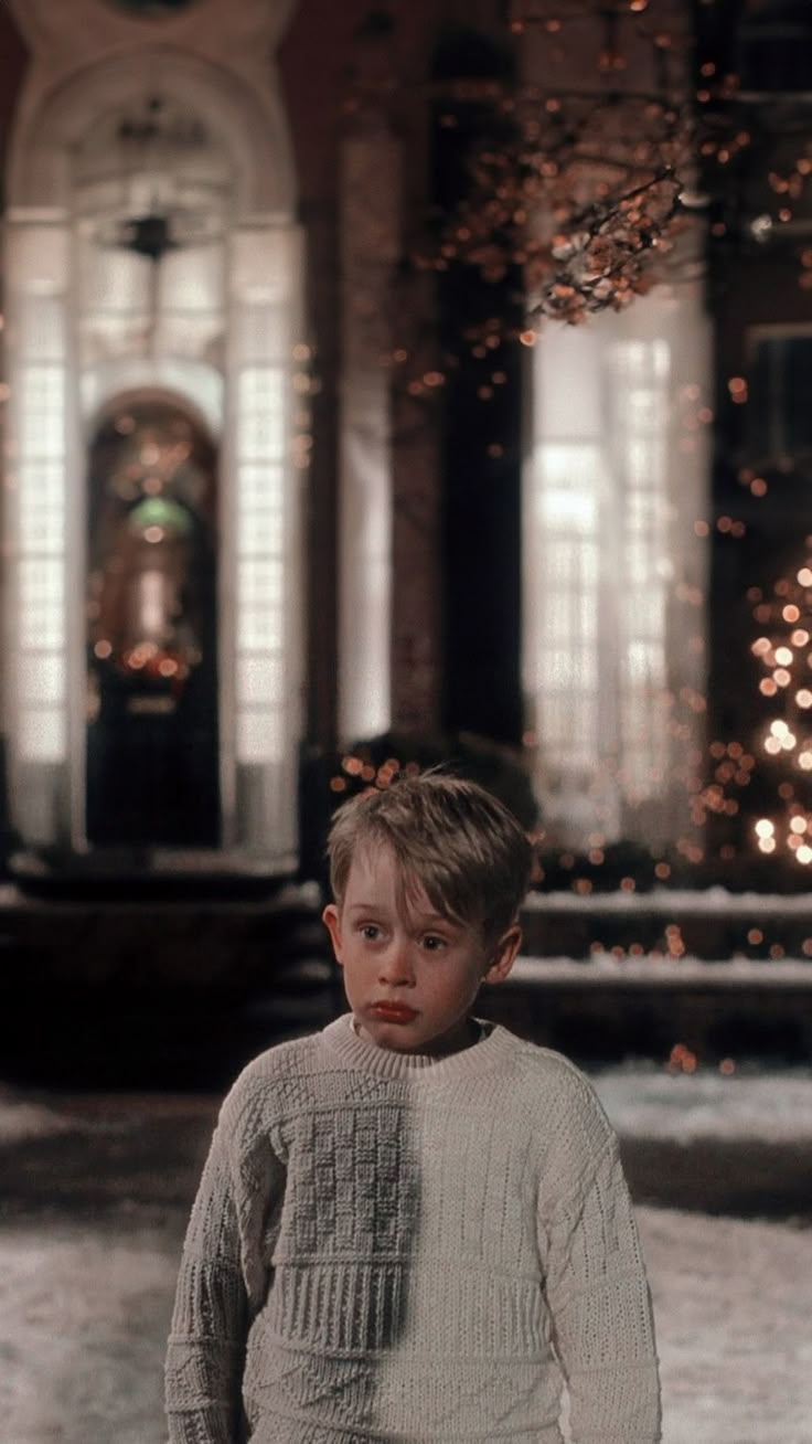 a young boy standing in front of a building with lights on the ceiling and windows