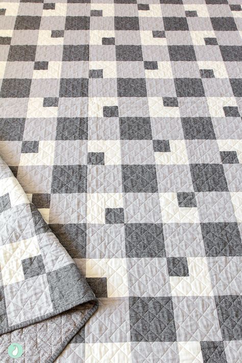 a gray and white checkered quilt on top of a bed next to a pillow