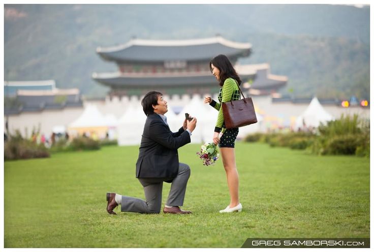 a man kneeling down next to a woman on top of a lush green field with a building in the background