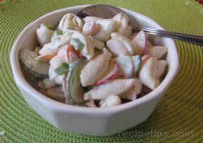 a white bowl filled with pasta and vegetables on top of a green place mat next to a spoon