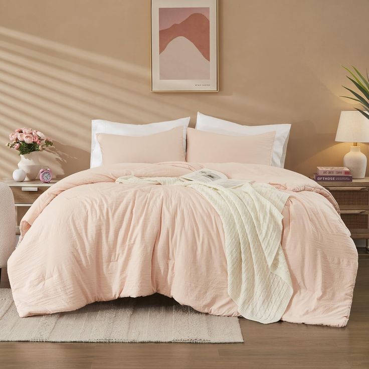 a bed with pink comforter and pillows in a beige room next to a white chair