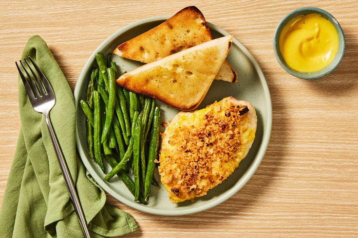 a white plate topped with green beans and bread next to a bowl of mustard sauce