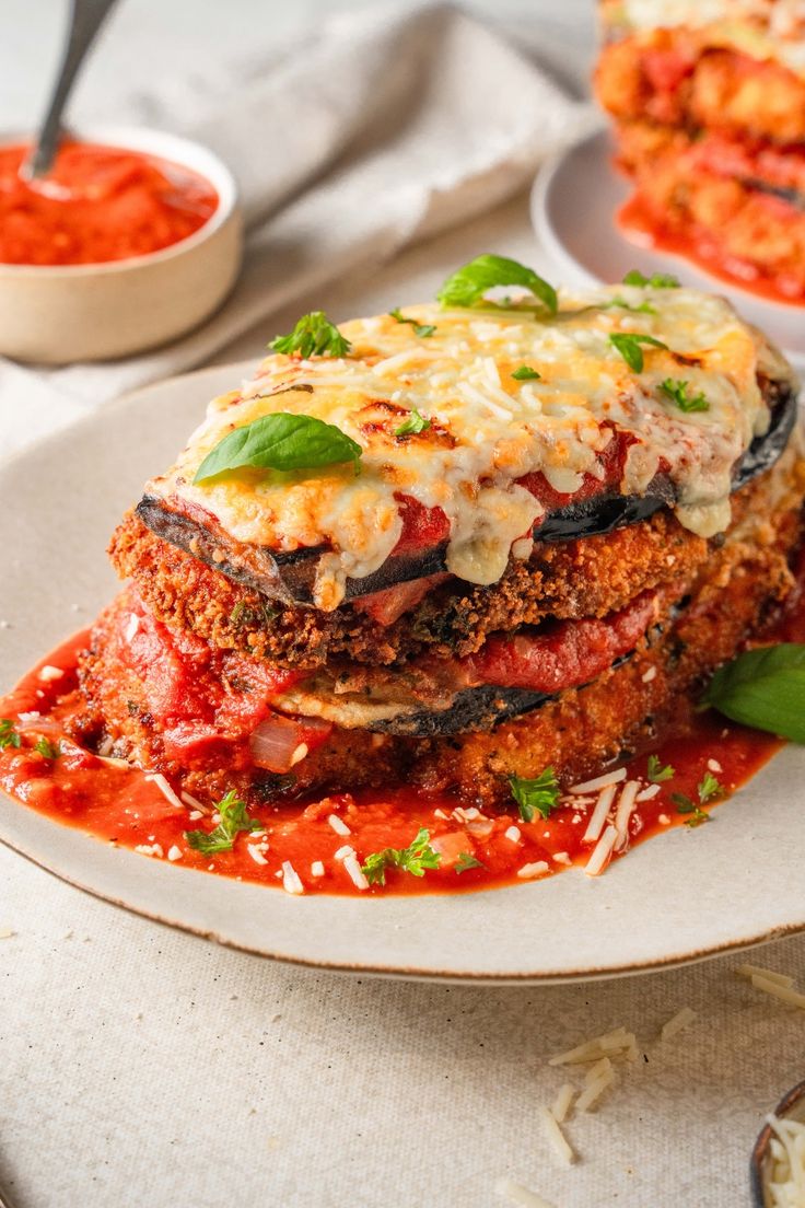 a white plate topped with lasagna covered in sauce and garnished with basil