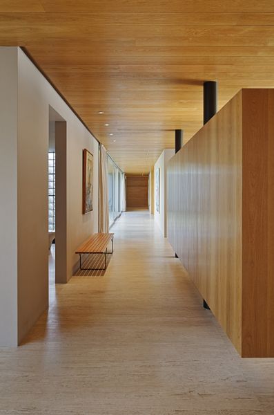 a long hallway with wooden walls and benches on either side, leading to another room