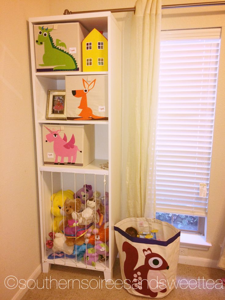 a white book shelf filled with toys next to a window in a child's room