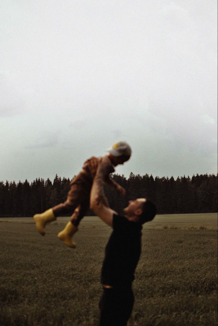 a man holding a child up in the air with trees in the back ground behind him