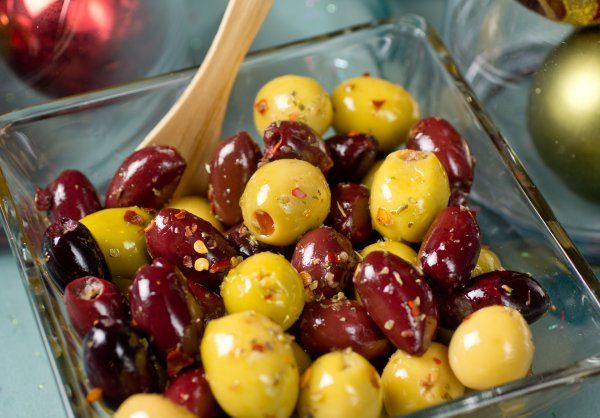 olives in a glass dish with a wooden spoon next to christmas ornaments and baubles