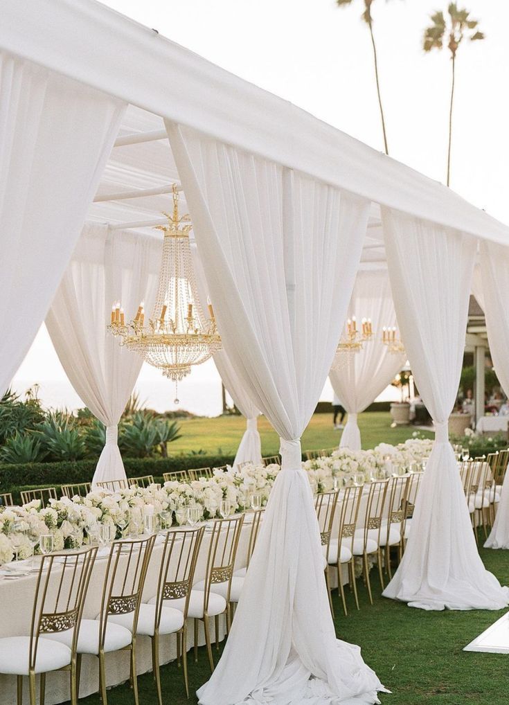 an outdoor wedding setup with white draping and chandeliers