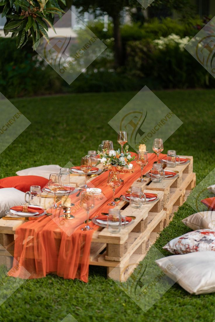 an outdoor table set up with orange linens and place settings for dinner on the grass