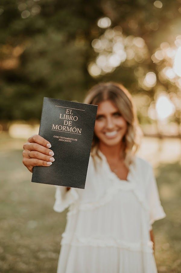 a woman holding up a book in front of her face with the title el libro de mormon written on it