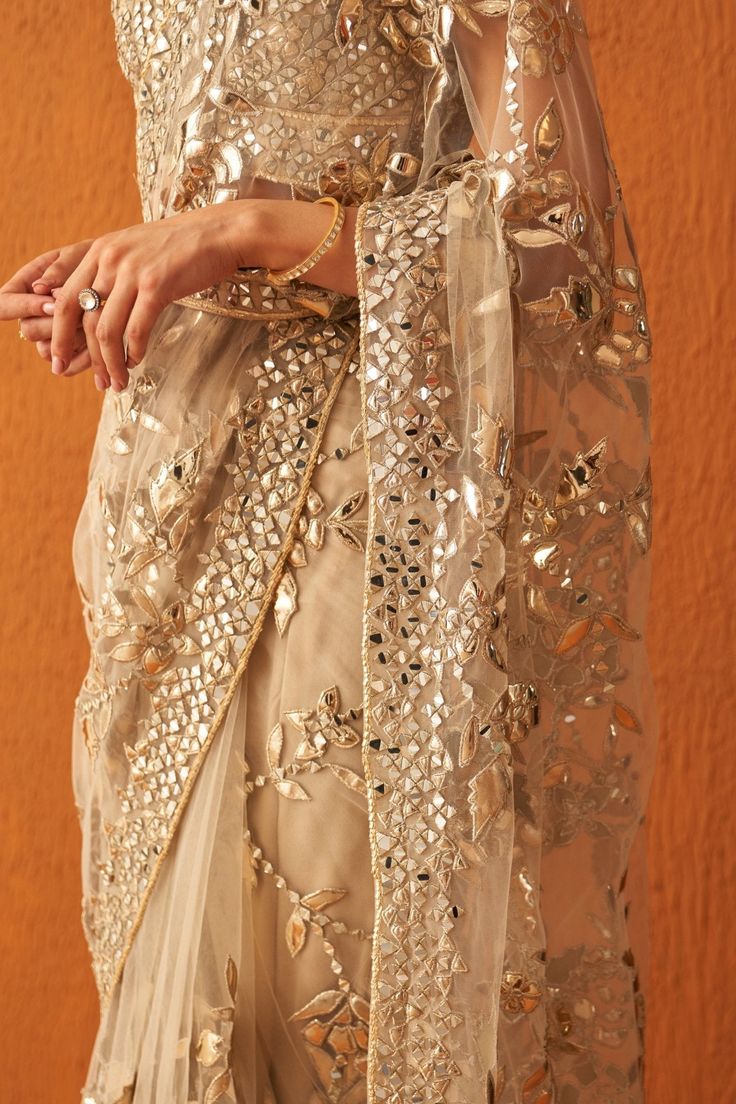 Features a gold saree set in soft net embellished with leather applique and mirrorwork in vine pattern and gold zari along the border. Teamed with a V-neck embellished bustier with tasseled tie-up and a belt.Composition : Saree: Net, Blouse: GeorgetteCare: Dry Clean Only and Vacuum Storage All products can be customised for sleeves, length of blouse and neck design Delivery : 4-6 weeks as the product is hand crafted. Check Size Guide or choose MySize for free customisation (All Sizes above XL can be made at 15% additional cost) For more information and sizes please contact fabiliciousfashion@gmail.com or visit our Copenhagen studio.About the Designer : Angad Singh's journey in the world of fashion started with at an early age as he grew up in a family business that was immersed in couture. Traditional Embellished Pre-draped Saree For Festive Season, Gold Pre-draped Saree With Intricate Embroidery For Reception, Traditional Organza Pre-draped Saree With Sequins, Festive Gold Embellished Pre-draped Saree, Elegant Pre-draped Kundan Saree For Party, Festive Gold Pre-draped Saree With Mirror Work, Gold Pre-draped Saree With Sheer Dupatta For Eid, Pre-draped Saree With Mirror Work For Celebration, Glamorous Organza Pre-draped Saree With Zari Work