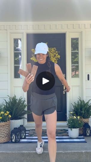 a woman is running in front of a house with her cell phone and hat on