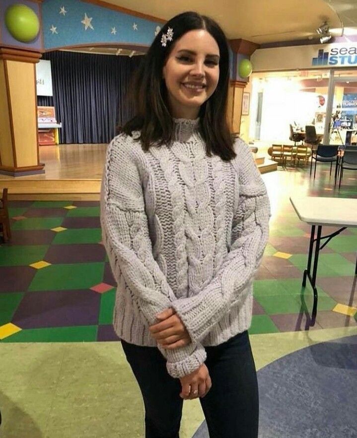 a woman standing in front of a table wearing a gray sweater and black leggings