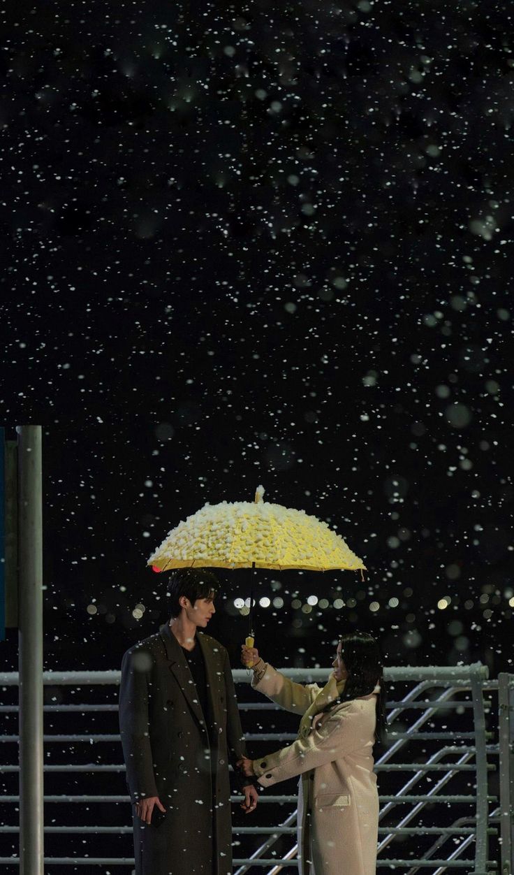 two people standing under an umbrella in the rain with snow falling all around them and one person holding it up