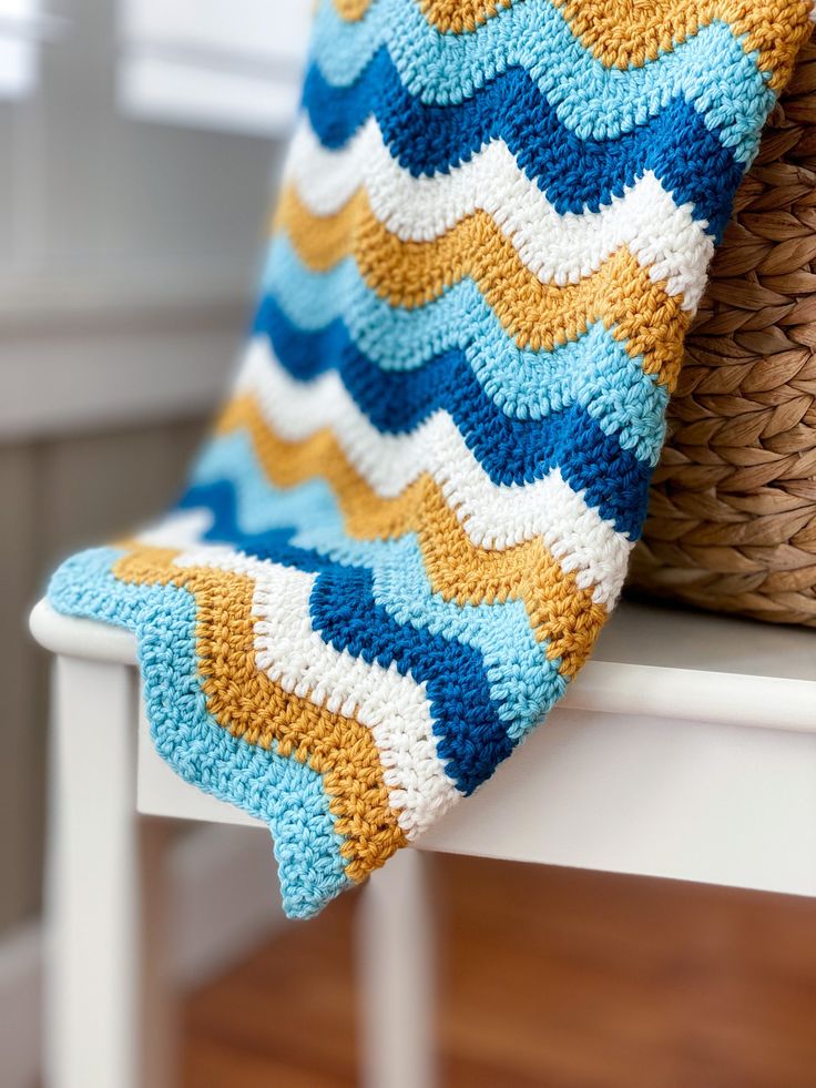 a crocheted blanket sitting on top of a white chair next to a basket