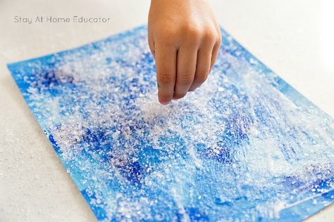 a child's hand on top of a blue piece of paper that has snow flakes all over it