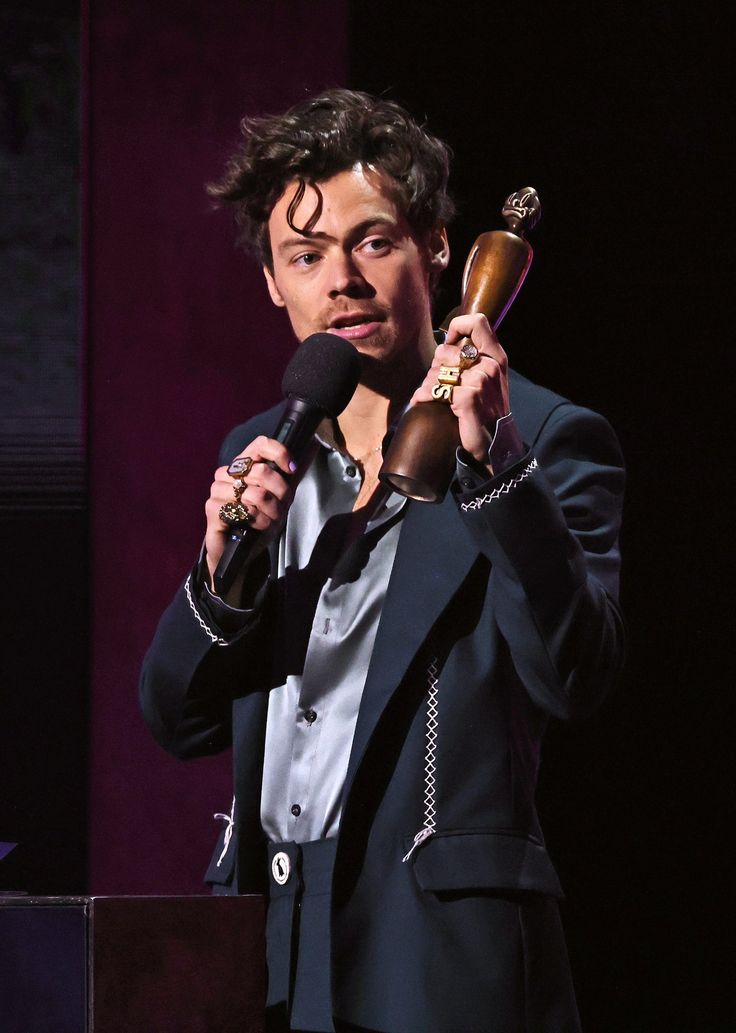 a man holding a microphone in his right hand and wearing a suit on the other