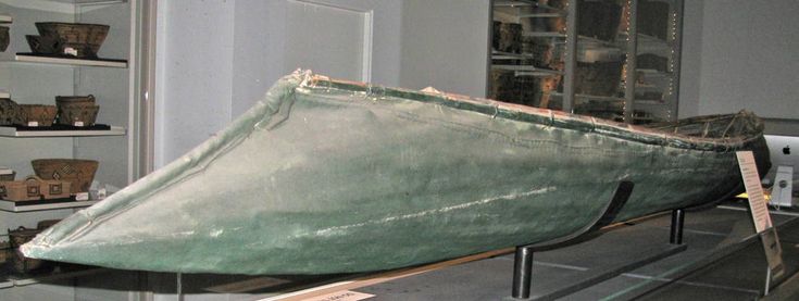 a green boat is on display in a glass case with shelves behind it and other items