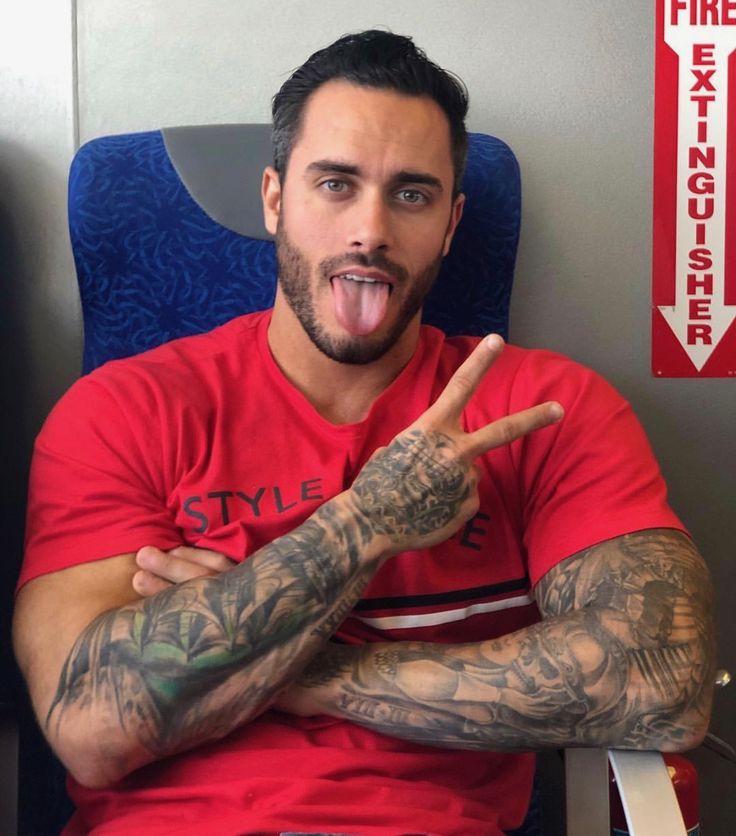 a man with tattoos on his arm sitting in a chair and making the v sign