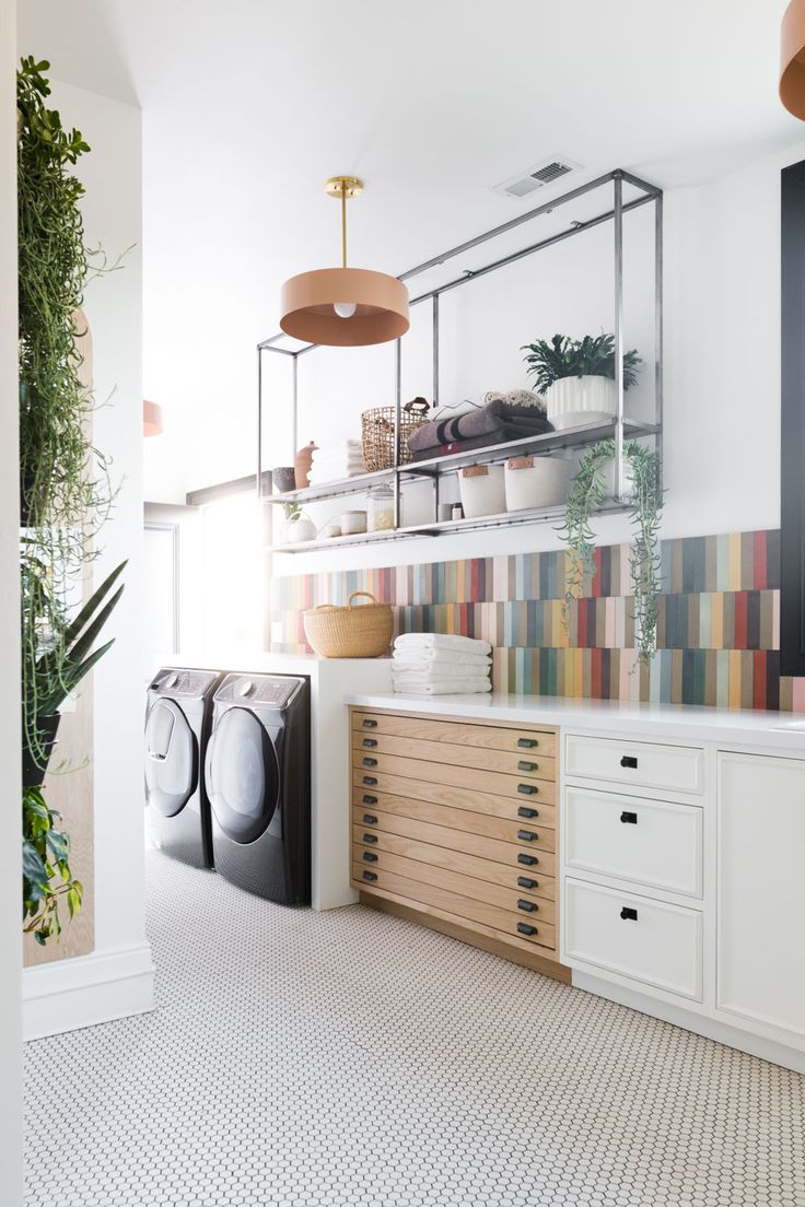 a laundry room with white cabinets and colorful tiles on the wall, hanging planters