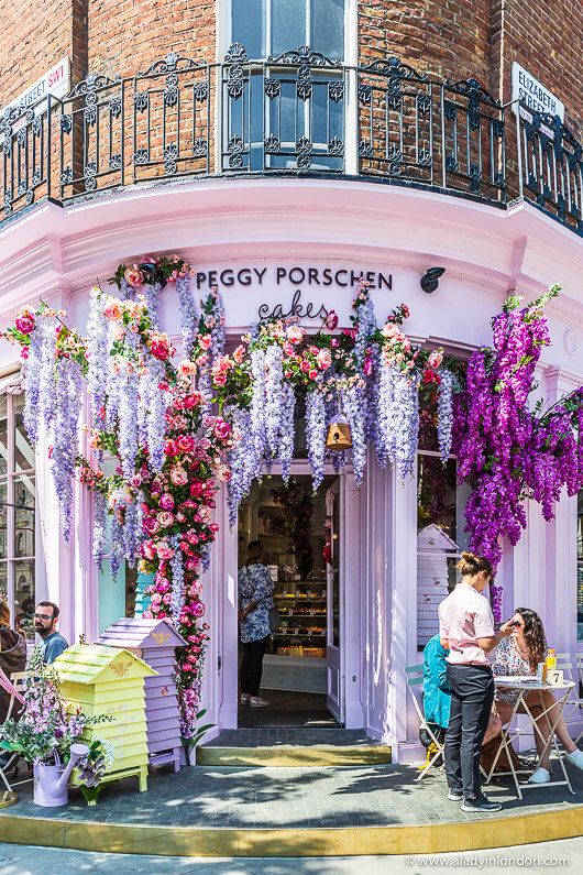 people sitting at tables in front of a building with purple flowers on the outside wall