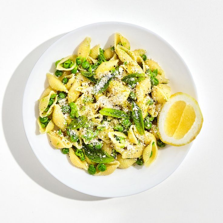 a white plate topped with pasta and broccoli covered in sauce next to a lemon wedge