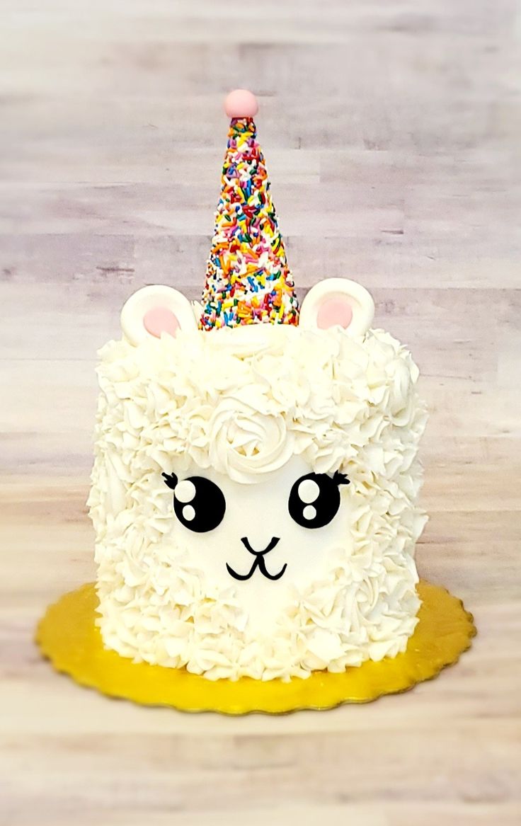 a white cake with sprinkles and a llama wearing a party hat