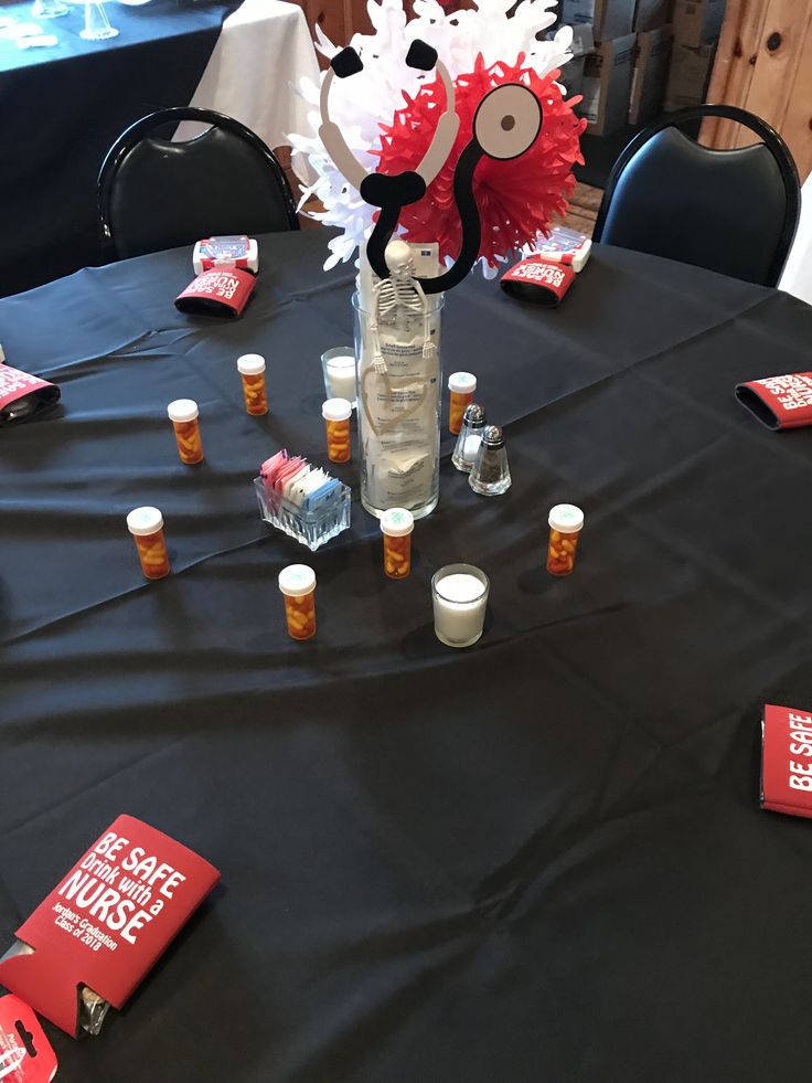 a table topped with lots of bottles and cups filled with liquid on top of a black cloth covered table