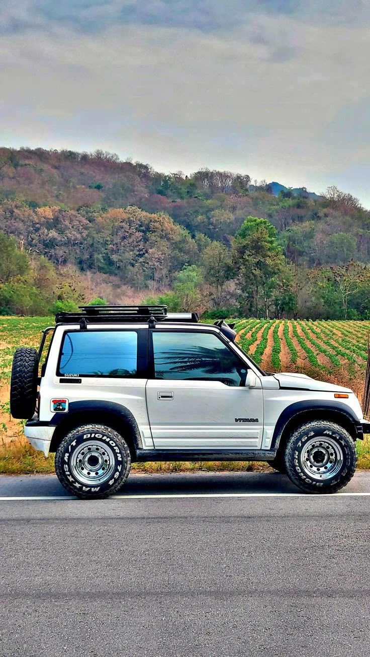 a white jeep parked on the side of a road next to a cornfield with trees