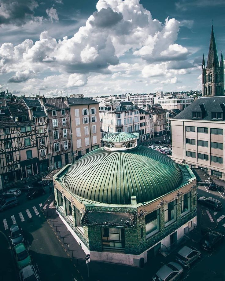 an old building with a green roof in the middle of a large city under a cloudy sky