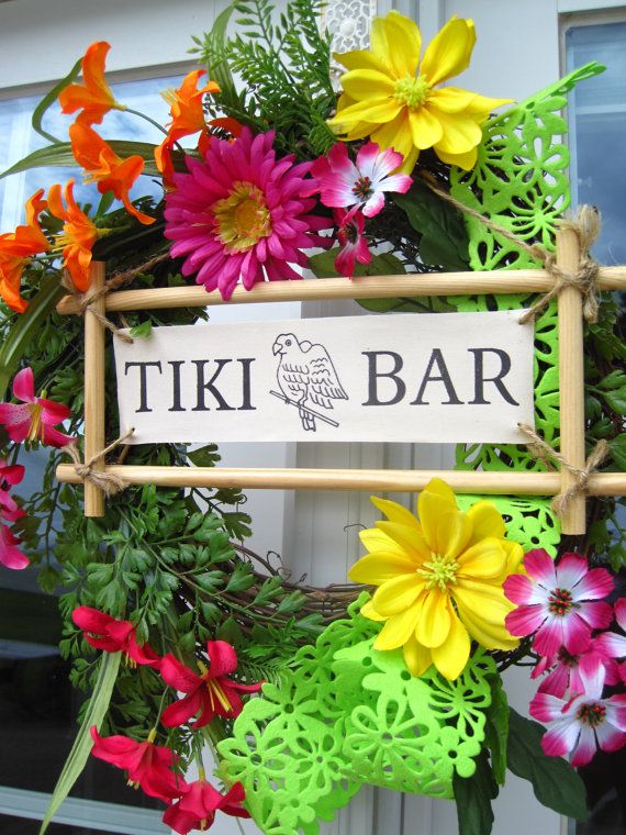 a sign that says tiki bar hanging from the side of a door surrounded by flowers