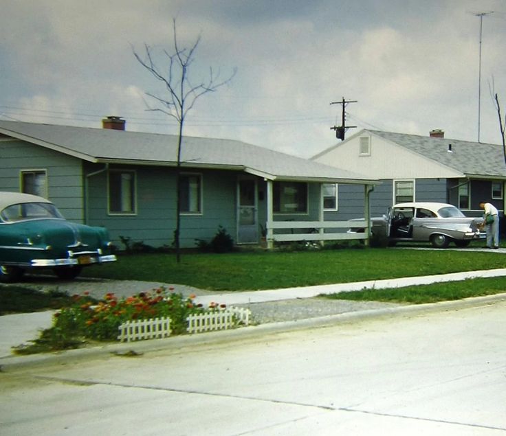 two cars parked in front of houses on the side of the road with grass and flowers