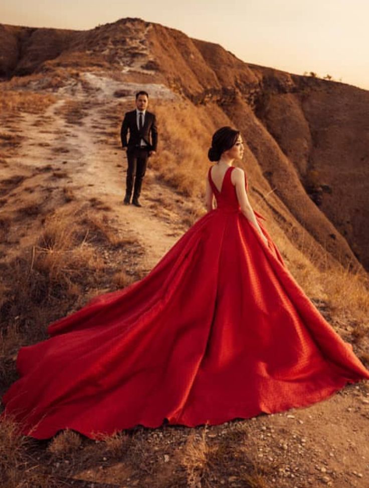 a woman in a red dress standing next to a man in a suit on top of a hill