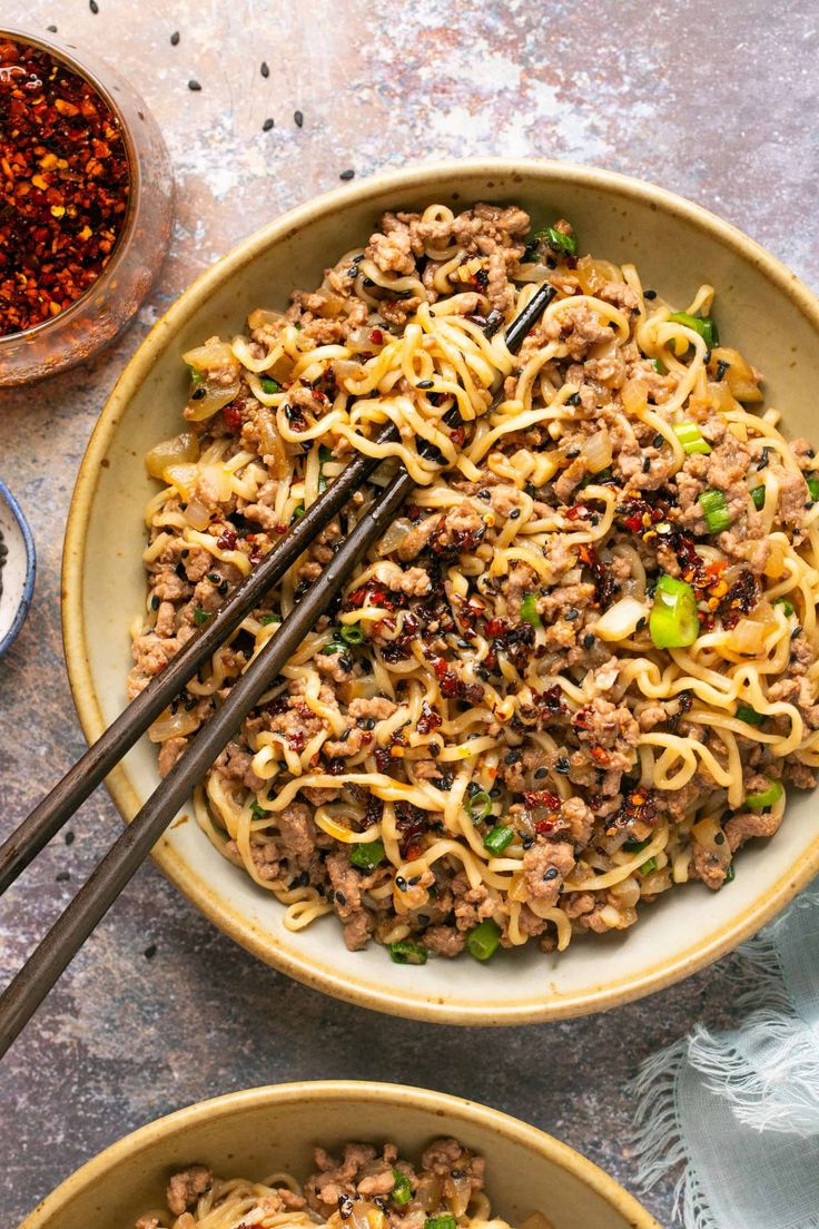 two bowls filled with noodles and meat on top of a table next to some chopsticks