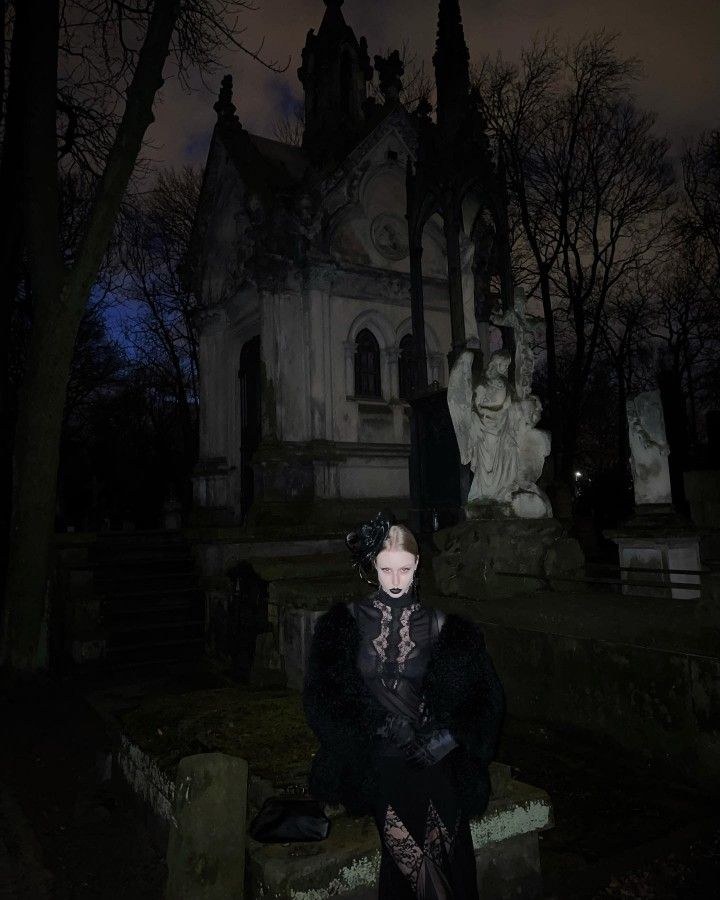 a woman standing in front of a cemetery at night with her hands on her hips