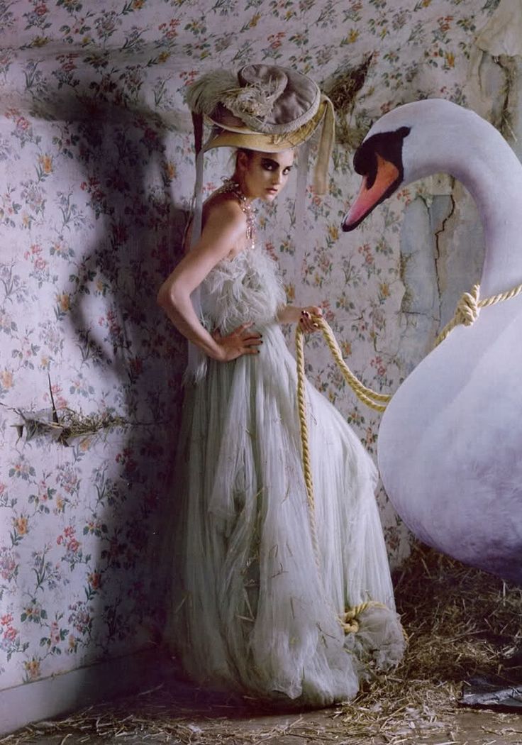 a woman standing next to a swan in a room with floral wallpaper and flowers on the walls