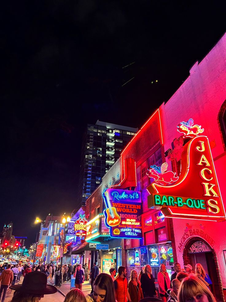 people are walking down the street in front of neon signs and buildings at night time