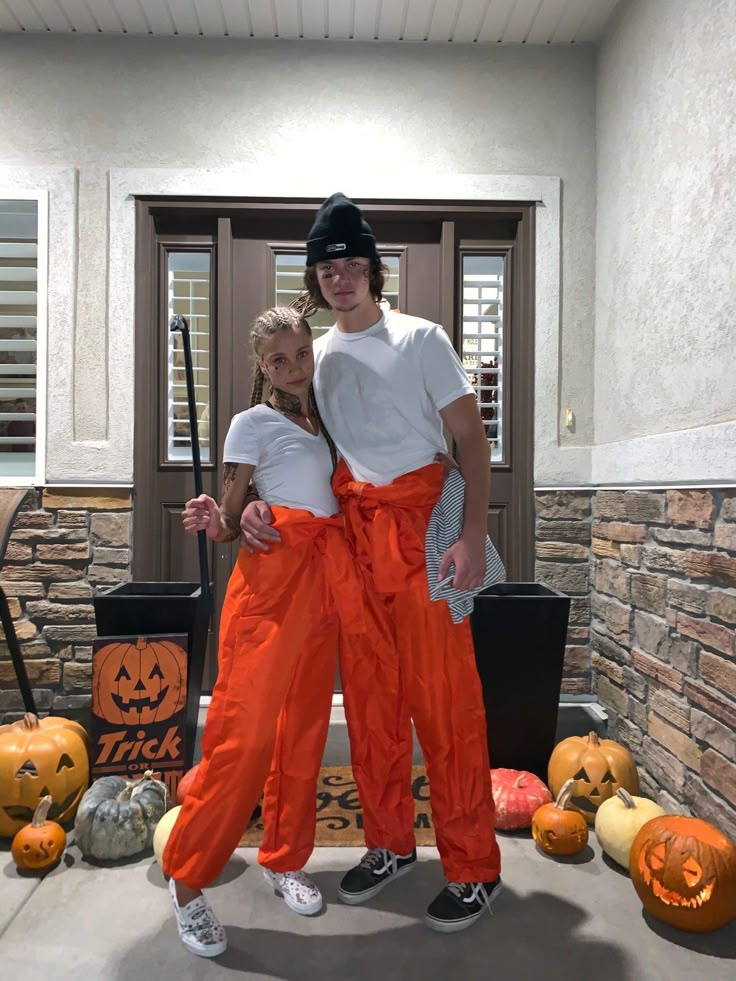 a man and woman in orange pants standing next to each other with pumpkins behind them