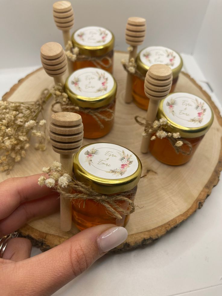 a hand holding a jar of honey on top of a wooden slice with other jars in it