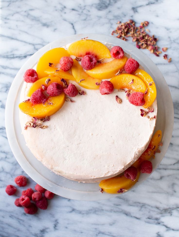 a white cake topped with fresh fruit on top of a marble counter next to raspberries