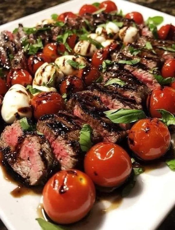 grilled steak with cherry tomatoes, mozzarella and basil on a white plate