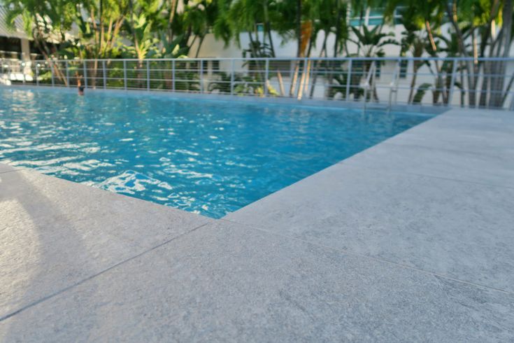 an empty swimming pool with palm trees in the backgrouds and blue water