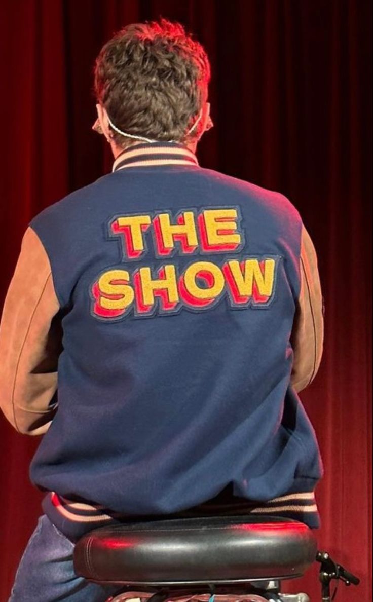 a man sitting on top of a chair in front of a red curtain with the show written on it