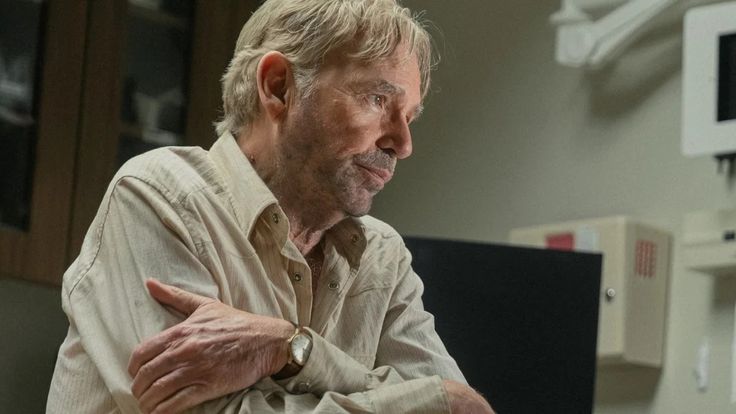 an older man sitting at a desk with his arms crossed and looking off to the side